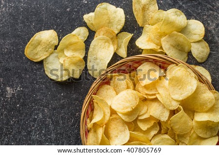 Crispy potato chips in a wicker bowl on old kitchen table Royalty-Free Stock Photo #407805769