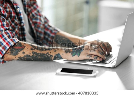 Young man with tattoo using laptop at the table