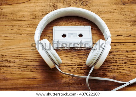 Retro compact cassette with rolls and white big headphones on wooden table texture