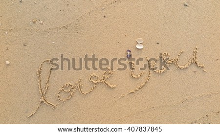 written words "love you" on sand of beach