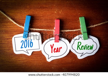Paper speech bubbles with text 2016 Year Review hanging on the line against dark wooden background.