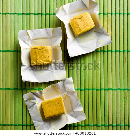 Dehydrated condiment bouillon stock cube salty meat and vegetables aromatic yellow spice, ingredient single whole portion wrapped and open in paper pack , view from above.