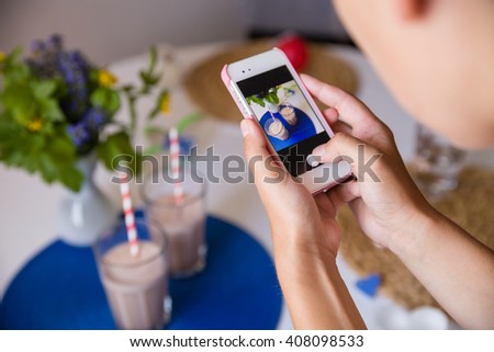 Woman taking photo of many glasses of fresh cold vanilla and chocolate smoothies with straws on table with flowers. Telephone photo of table setting for breakfast. Healthy snacks. Drinks for health.