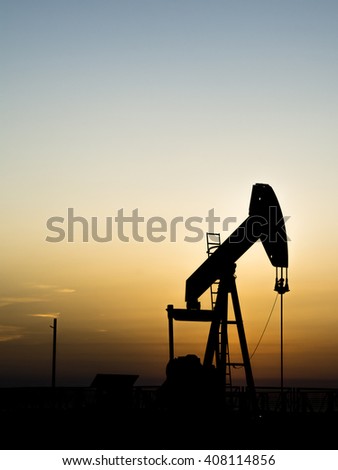 Sunset and silhouette of crude oil pump in oilfield