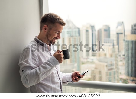 Handsome young businessman drinking coffee and holding a mobile phone.