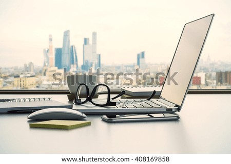 Sideview of office desk with laptop, glasses and other items on Moscow city background