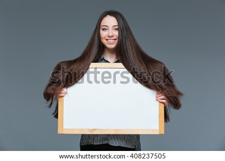 Smiling woman with long hair holding blank board over gray background
