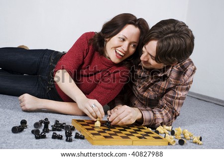 Happy young couple lying on carpet, playing chess.