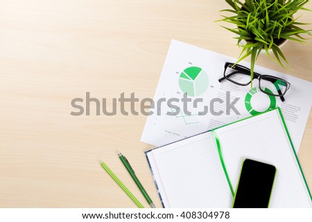 Office desk workplace with charts, phone, plant and notepad on wooden table. Top view with copy space