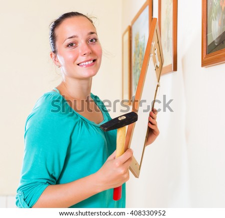 Ordinary young girl with picture and hammer in her hand at house