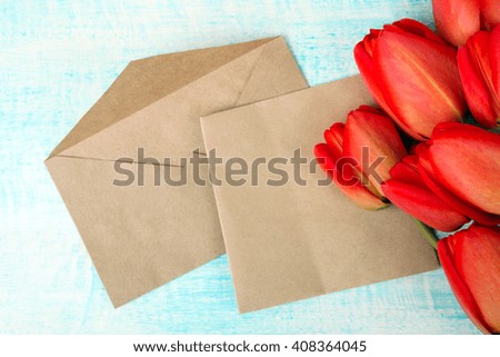 a fragrant bouquet of red tulips with envelopes for letters on a blue wooden background