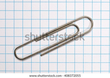 metallic paper clip over a white paper with blue squares