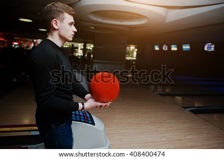 Young man holding a bowling ball standing against bowling alleys with ultraviolet light.