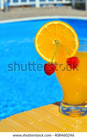 Cocktail with orange and cherry near the swimming pool on the background of the water.
