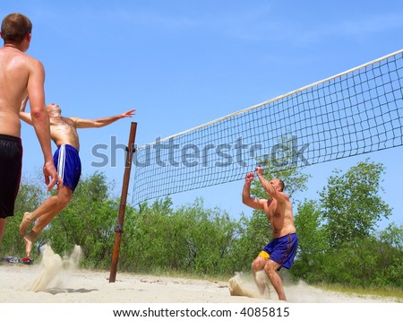 Three men playing beach volleyball - one watches, one spikes, one prepares to block. Shot near Dnieper river, Ukraine.