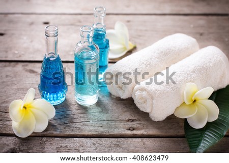 Spa or wellness setting.  Bottles with oil, towels and white plumeria flowers on wooden background. Selective focus.