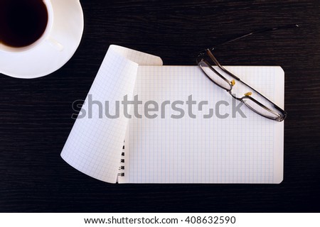 A cup of hot coffee, glasses, notebook on a wooden table. Place for text. Square image.