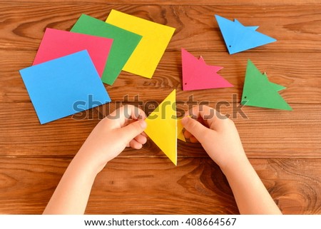 Origami colorful fish, paper sheets. Child holds an yellow origami fish in his hands. Brown wooden background 
