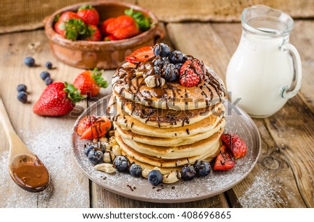 Original american pancakes with berries, roasted nuts and milk behind, rustic style photo, place for advertisment, topped with dark chocolate