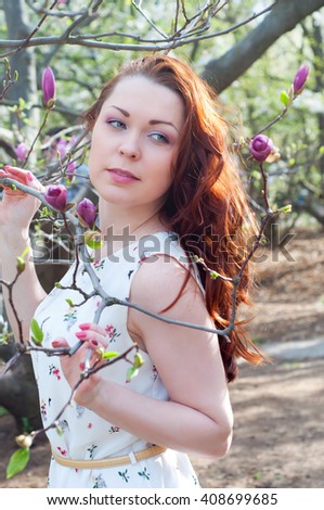 Redhead with green eyes in spring garden surrounded by pink magnolia flowers