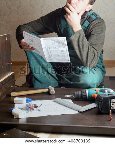 Frustrated man reading instruction and putting together self assembly furniture. DIY, new home and moving concept Royalty-Free Stock Photo #408700135