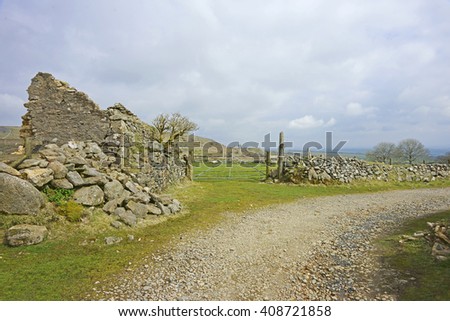 The ruins of an ancient Cottage near a country track running through Bodmin Moor with views across to the South Caradon mine and engine house in spring, Cornwall, England, UK