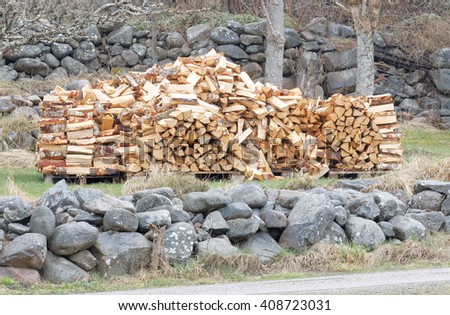Large stack of birch firewood. Rural stone wall behind and in front 
