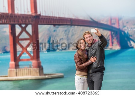 Happy young couple tourists taking selfie in San Francisco by Golden Gate Bridge, USA. Interracial young modern couple using smart phone. Asian woman, Caucasian man.