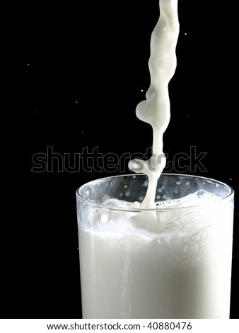 Stream of milk being poured in a glass on black background.