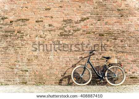 Black retro vintage bicycle with old brick wall and copy space. Retro bicycle with basket in front of the old brick wall. Old photo effect applied. Toned. 