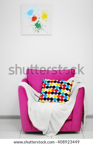 Pink armchair with blanket and pillow on light wall background