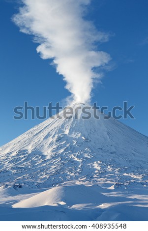 Winter volcanic landscape: highest active volcano of Eurasia - Klyuchevskoy Volcano (Klyuchevskaya Sopka), view of top of volcanic eruption: emission from crater plume of gas, steam and ashes.