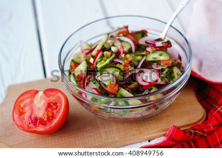 Fresh salad with cucumbers, tomatoes, radishes and onion in glass bowl on wooden background