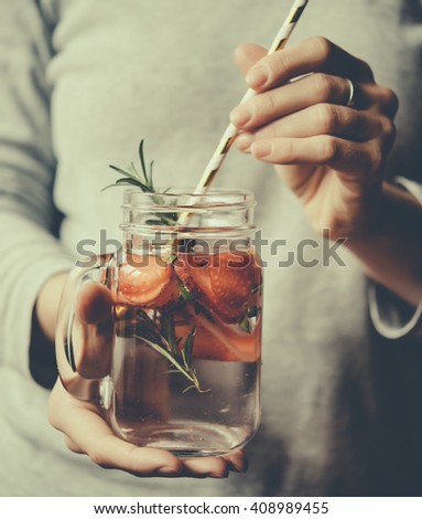 Hands holding retro glass jar of lemonade or cocktail with strawberry and rosemary. Toned picture