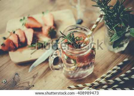 Retro glass jar of lemonade or cocktail with strawberry and rosemary on wooden table. Toned picture