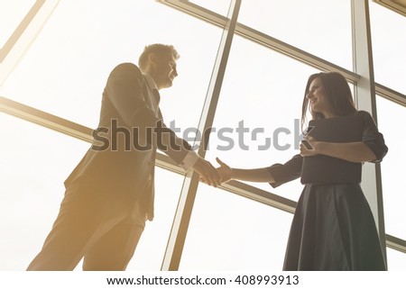 Business men and women shaking hands with a smile on the background of the large panoramic windows in a modern business center. Models dressed in a dark business suits.