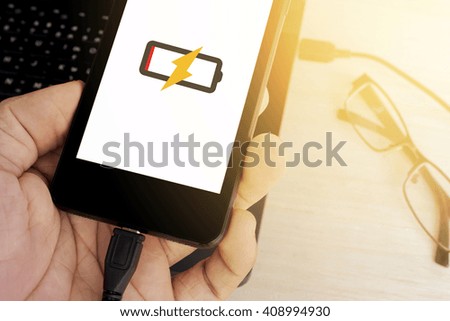 man's hand holding smart phone is charging from laptop sunlight color