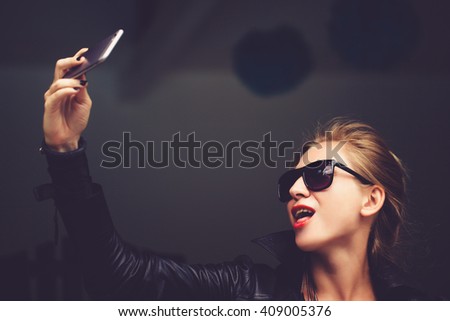 Young cute woman l hipster,sitting at cafe holding a smart phone,answering texts,calls,letters,posts photos in instagram,outdoor portrait,close up,elaborated and bracelets on the hands make selfie 