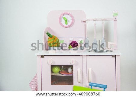 Pink kitchen children toy with utensils, food and a clock in a white background