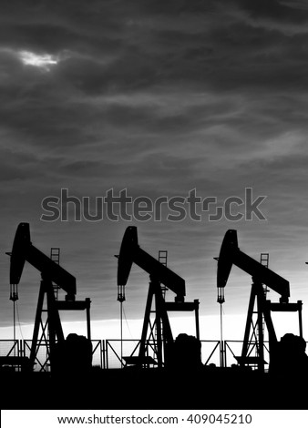 Cloudy sunset and silhouette of crude oil pumping units in oilfield - black and white