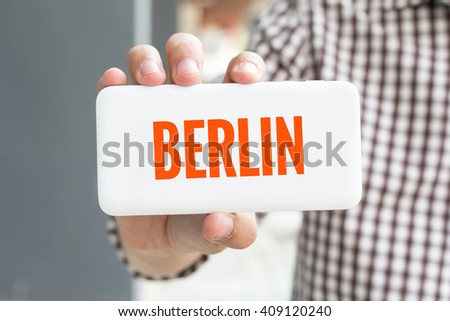 Man hand showing BERLIN word phone with  blur business man wearing plaid shirt.