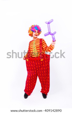 Funny playful girl clown in colorful wig holding a balloon dog, isolated on a white background. Clown in the costume