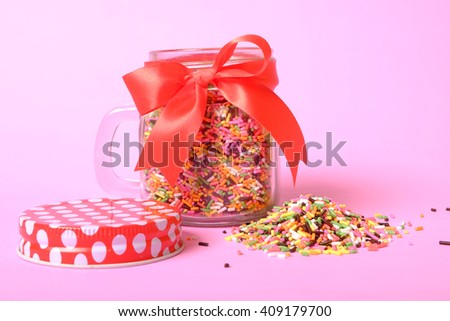 pile of colorful sugar sprinkles with jar on pink background, decoration for ice cream and bakery