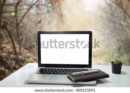 Front view of cup and laptop on table in Dry forest blurred background.