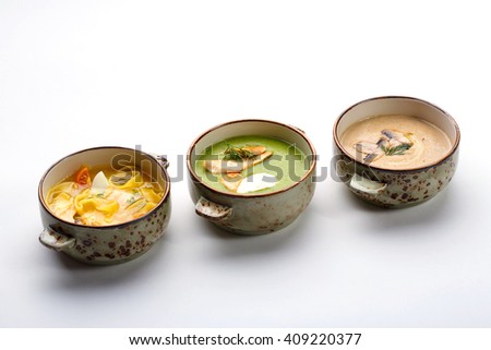 Three bowls with different soups: chicken fillet noodles soup, cream of broccoli soup with turkey and cream cheese, wild mushrooms soup. Royalty-Free Stock Photo #409220377