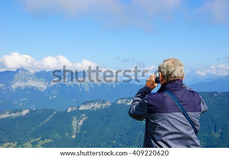 Senior unrecognizable man taking picture of idyllic summer landscape with Mont Blanc in Alps mountains. Annecy lake area (Haute-Savoie, France). 