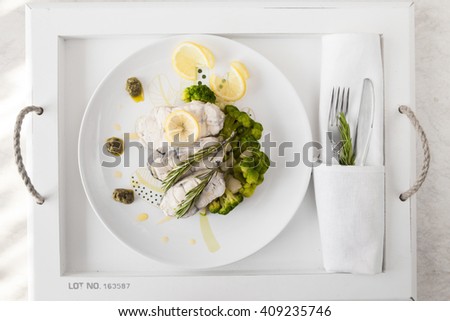 Fish fillet with vegetables and lemon and rosemary on white plate