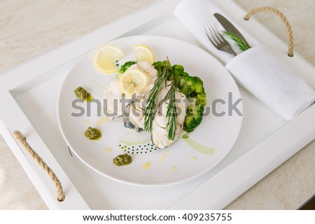 Fish fillet with vegetables and lemon and rosemary on white plate