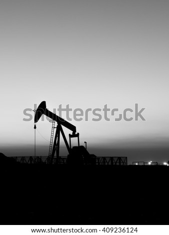 Sunset and silhouette of crude oil pumping unit in oilfield - black and white
