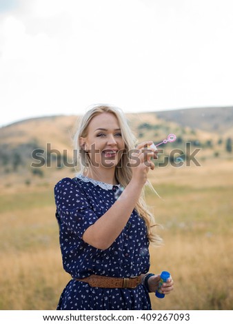 Portrait of a beautiful young woman blowing soap bubbles in the park on a sunny summer day